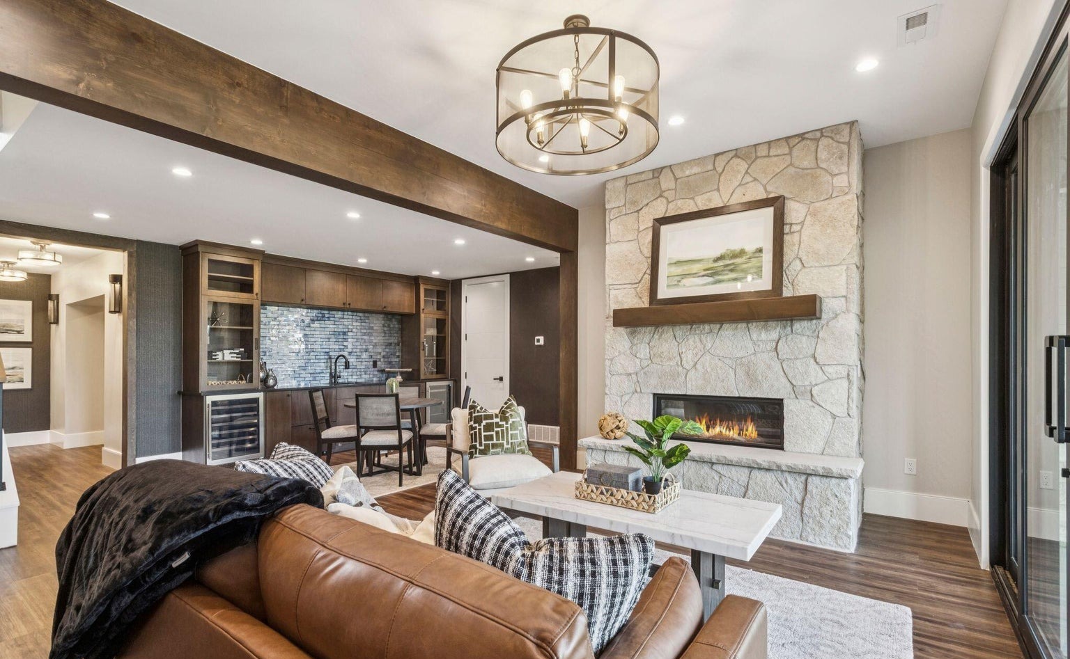 Living room with stone fireplace, exposed beams, and wet bar