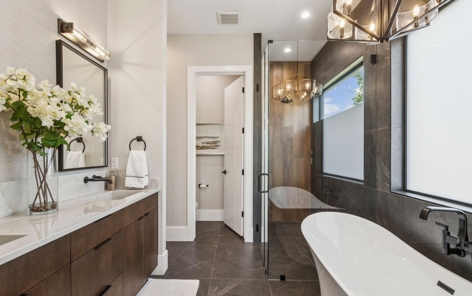 Freestanding soaking tub with dark tile surround and glass shower enclosure