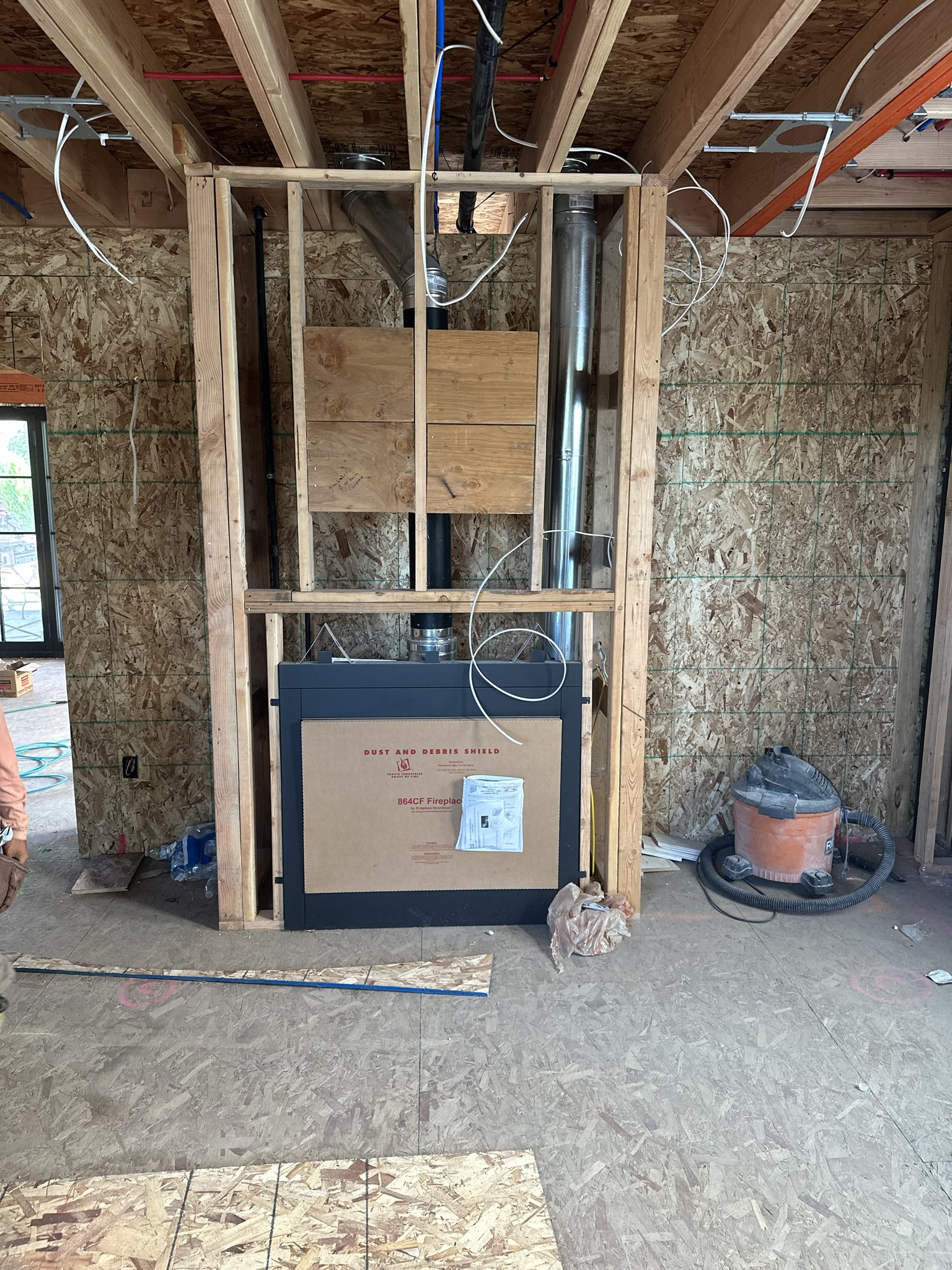 864CF gas fireplace unit being installed in framed chase — double-wall chimney pipe, proper clearances maintained, living room taking shape