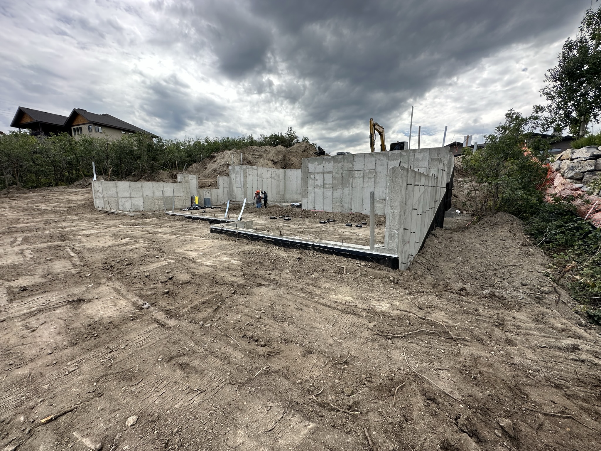 Poured concrete foundation walls with excavator on site, forms stripped, ready for waterproofing