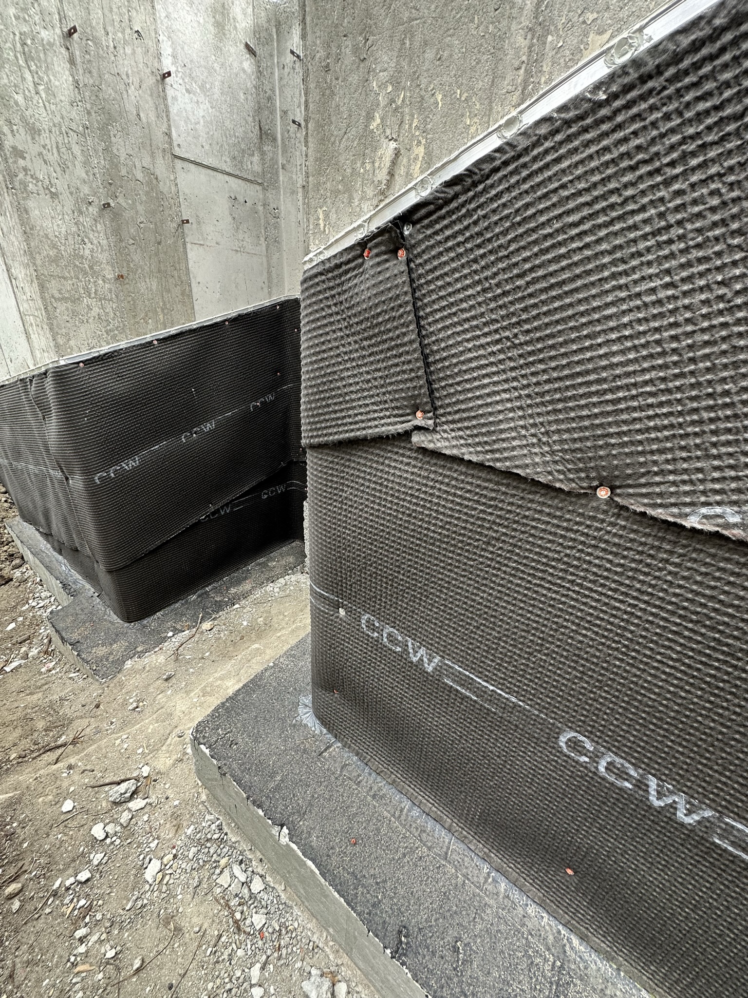 Close-up of CCW waterproofing membrane at foundation corner showing proper lapping and fastening technique