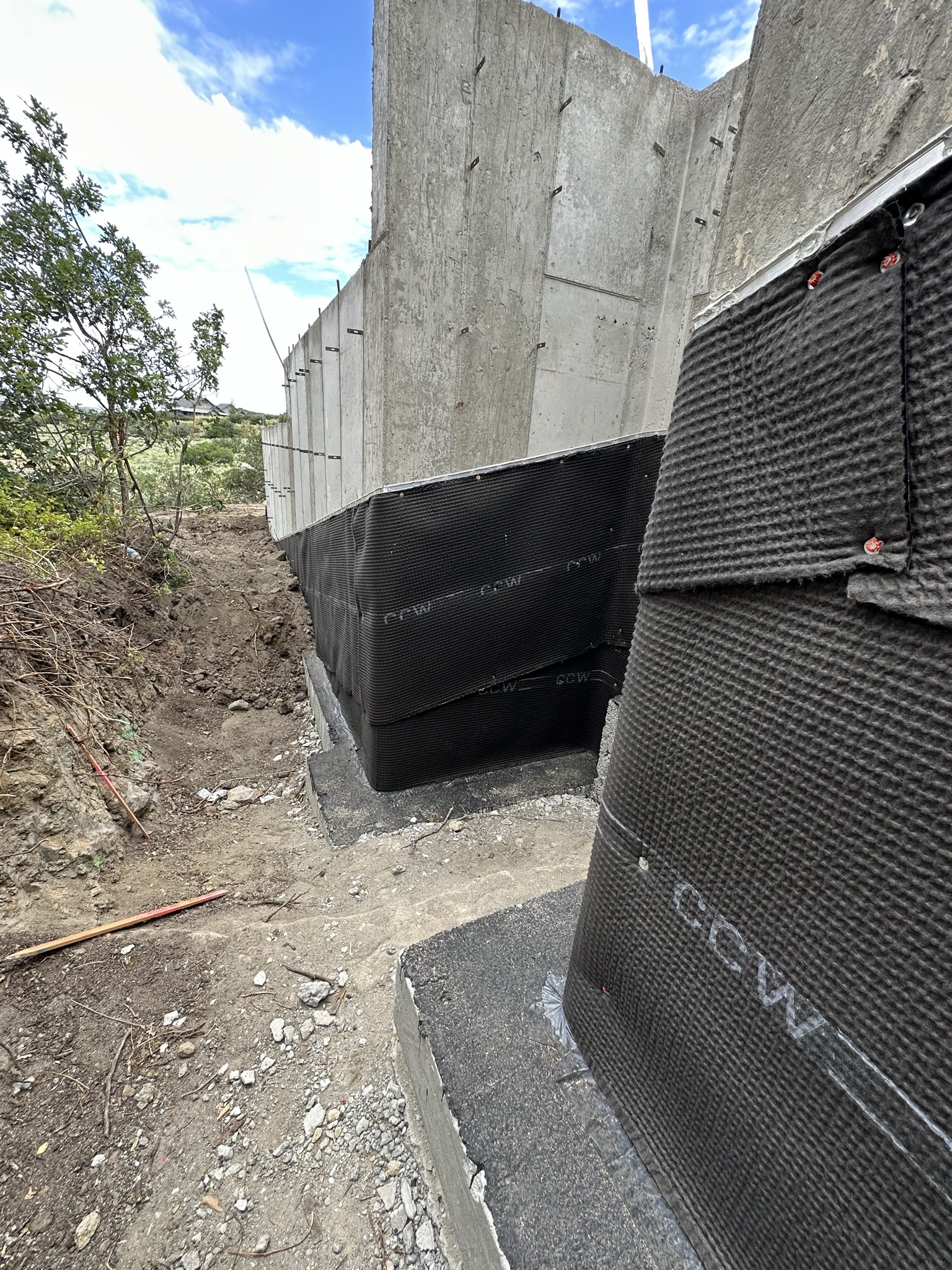 Exterior view of foundation wall with CCW membrane wrapping corners, excavated hillside visible