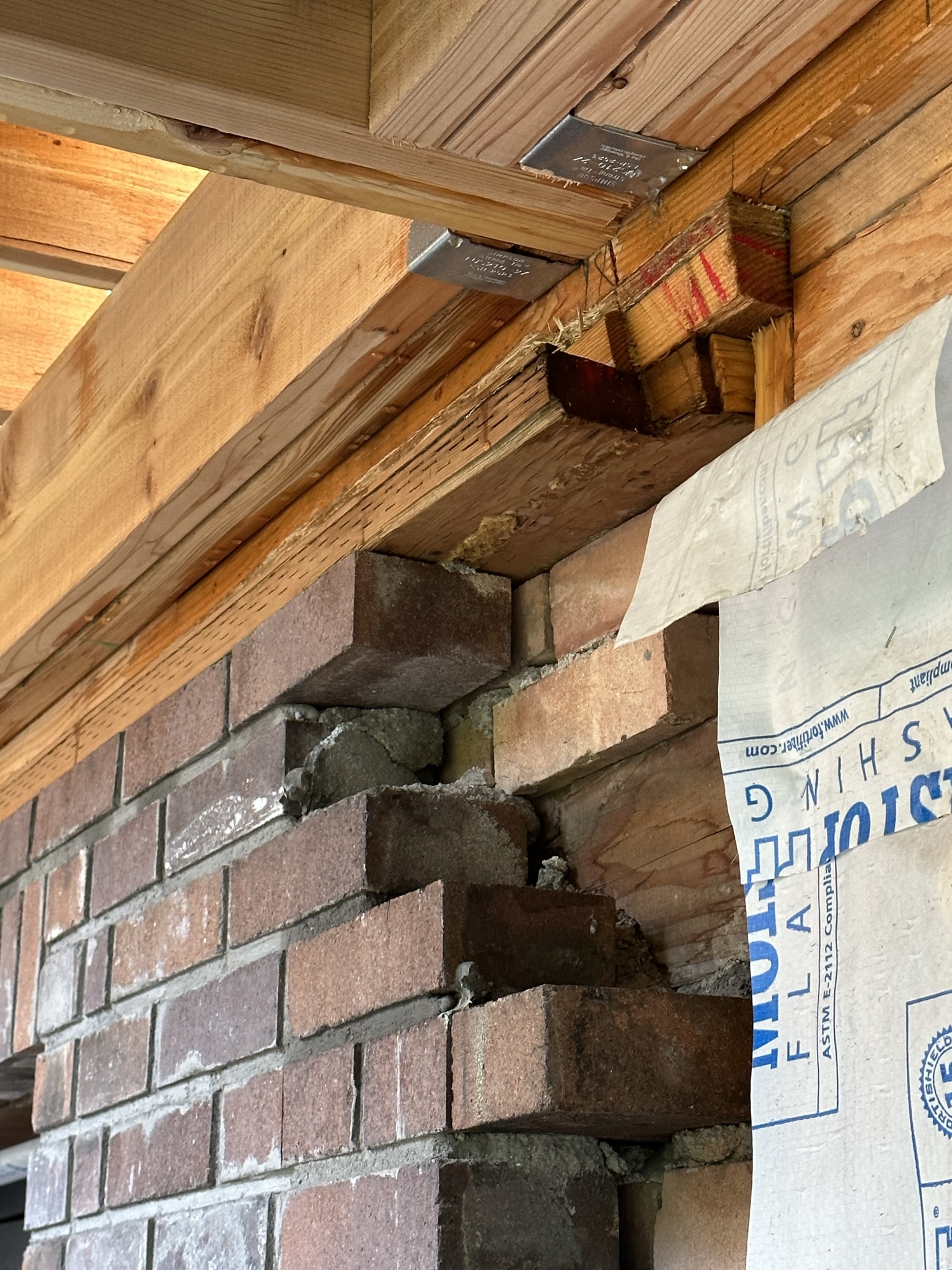 Close-up of new LVL beam connecting to existing brick wall with engineered metal joist hangers — critical structural connection point