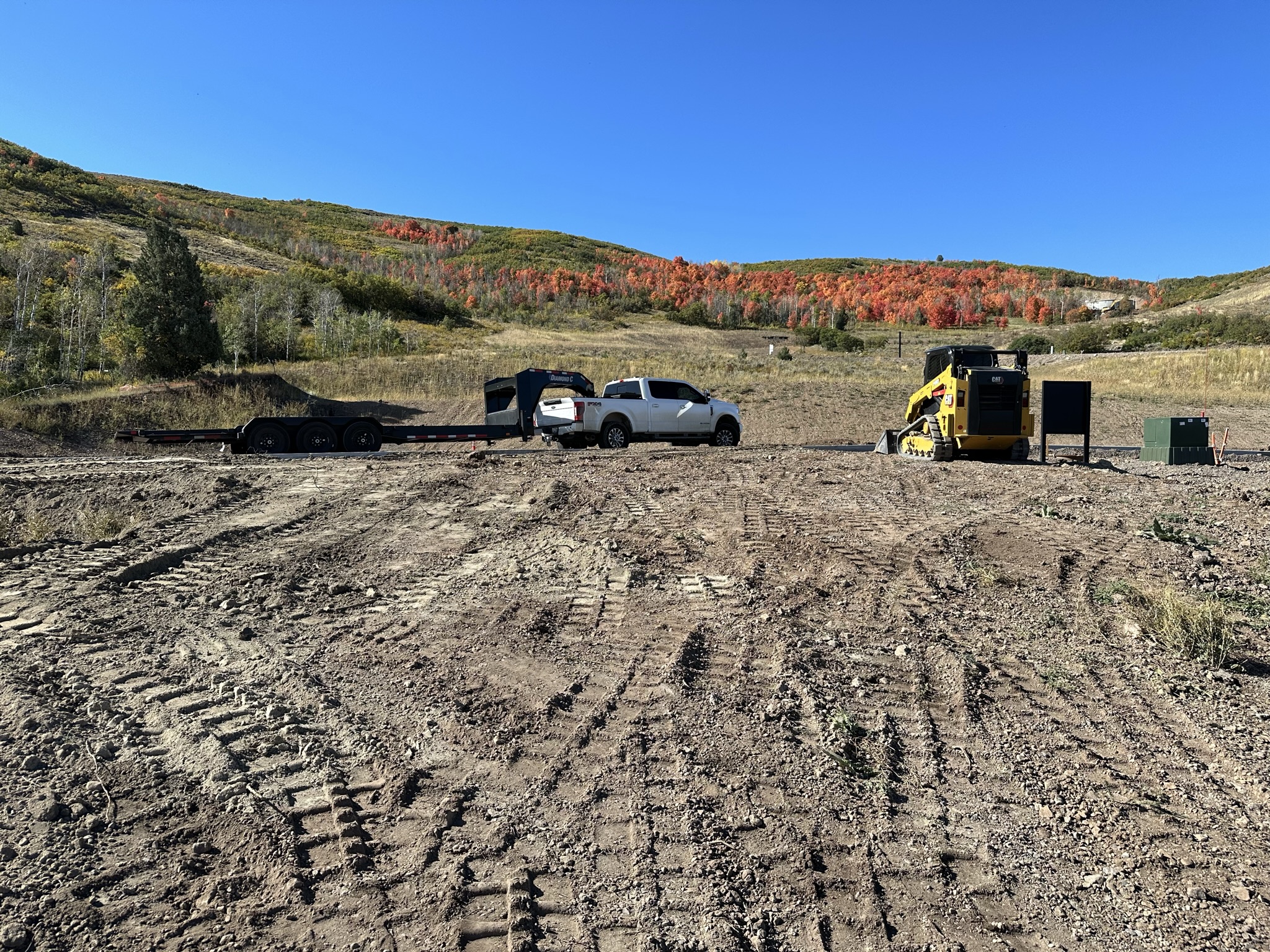 Raw mountain building lot with scrub oak, dirt, and construction equipment — Day 1 of the Park City Parade Home project