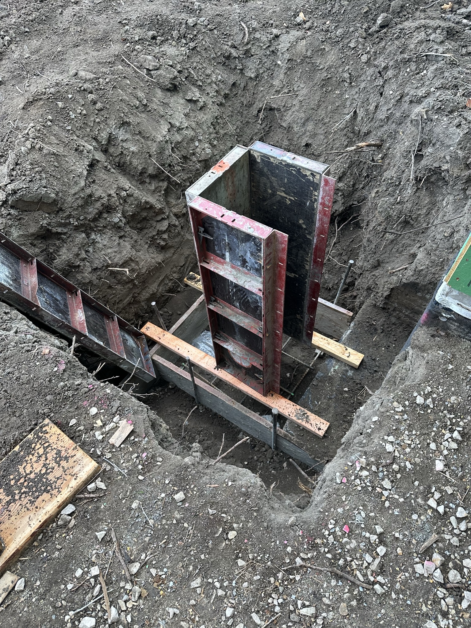 Steel foundation forms set in excavated trench, ready for concrete pour — the first permanent structure on the lot