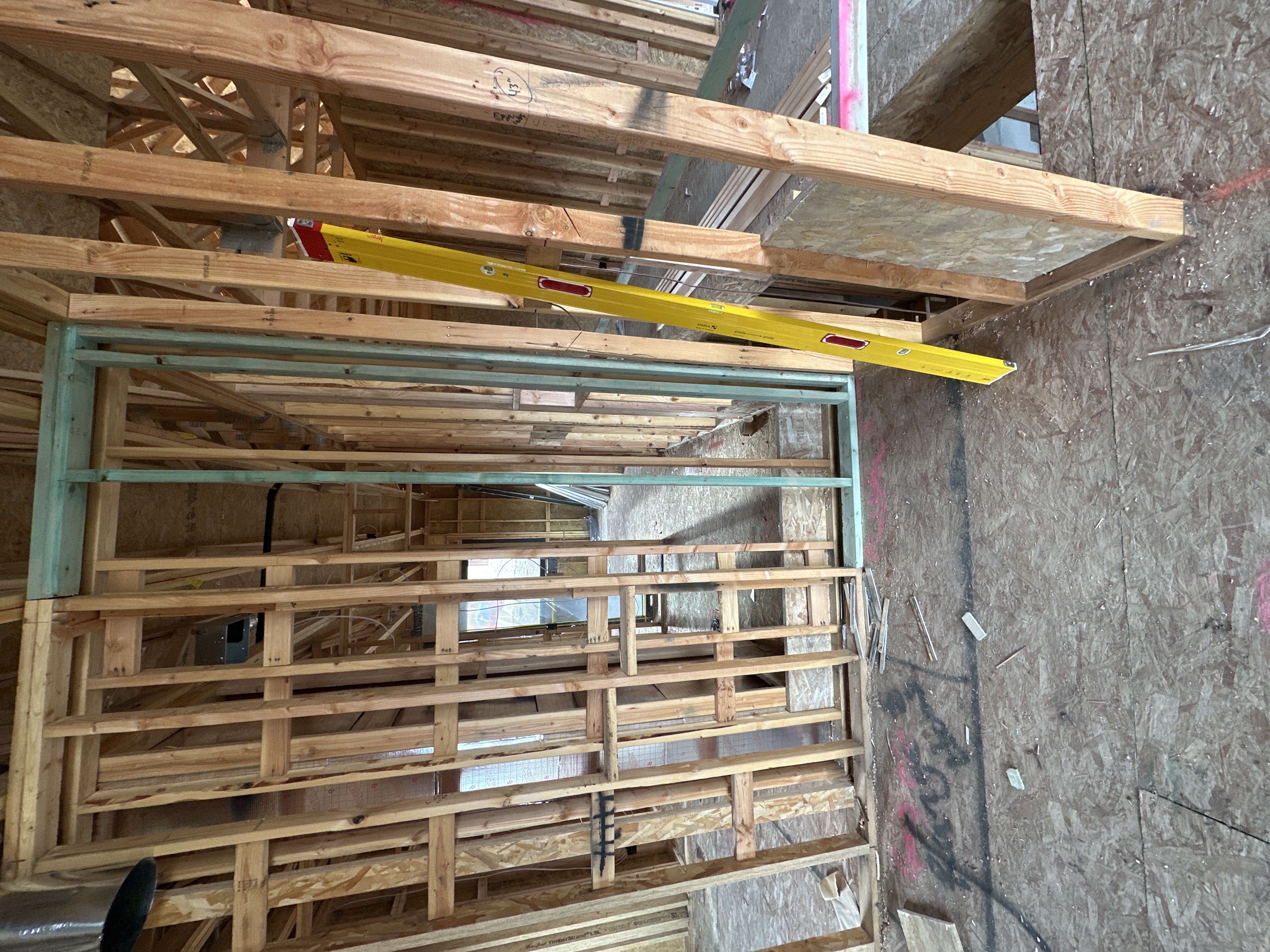 Interior framing detail — stud walls with yellow level, trusses overhead, OSB subfloor