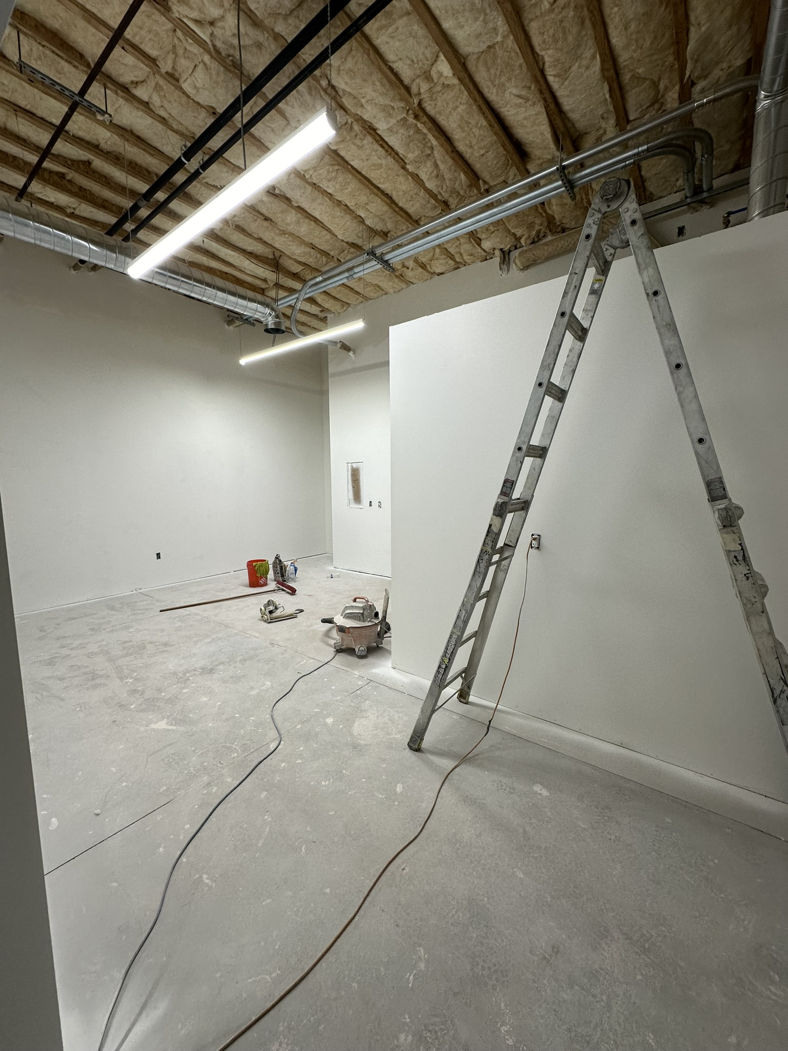 Basement level with drywall hung, HVAC ductwork in exposed ceiling, ladder and tools on concrete floor