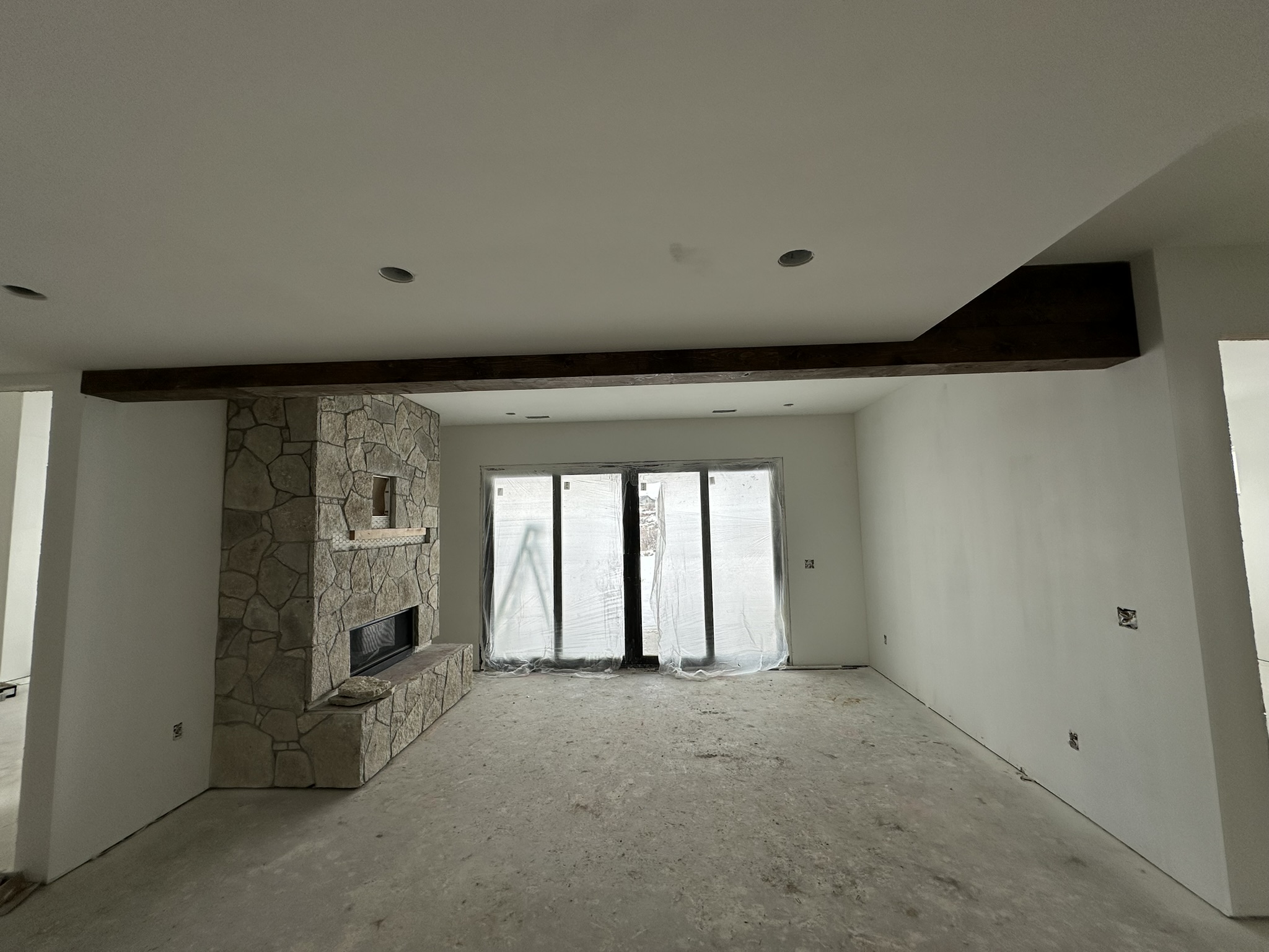 Great room during pre-finish phase — drywall, rough openings, and exposed ceiling structure