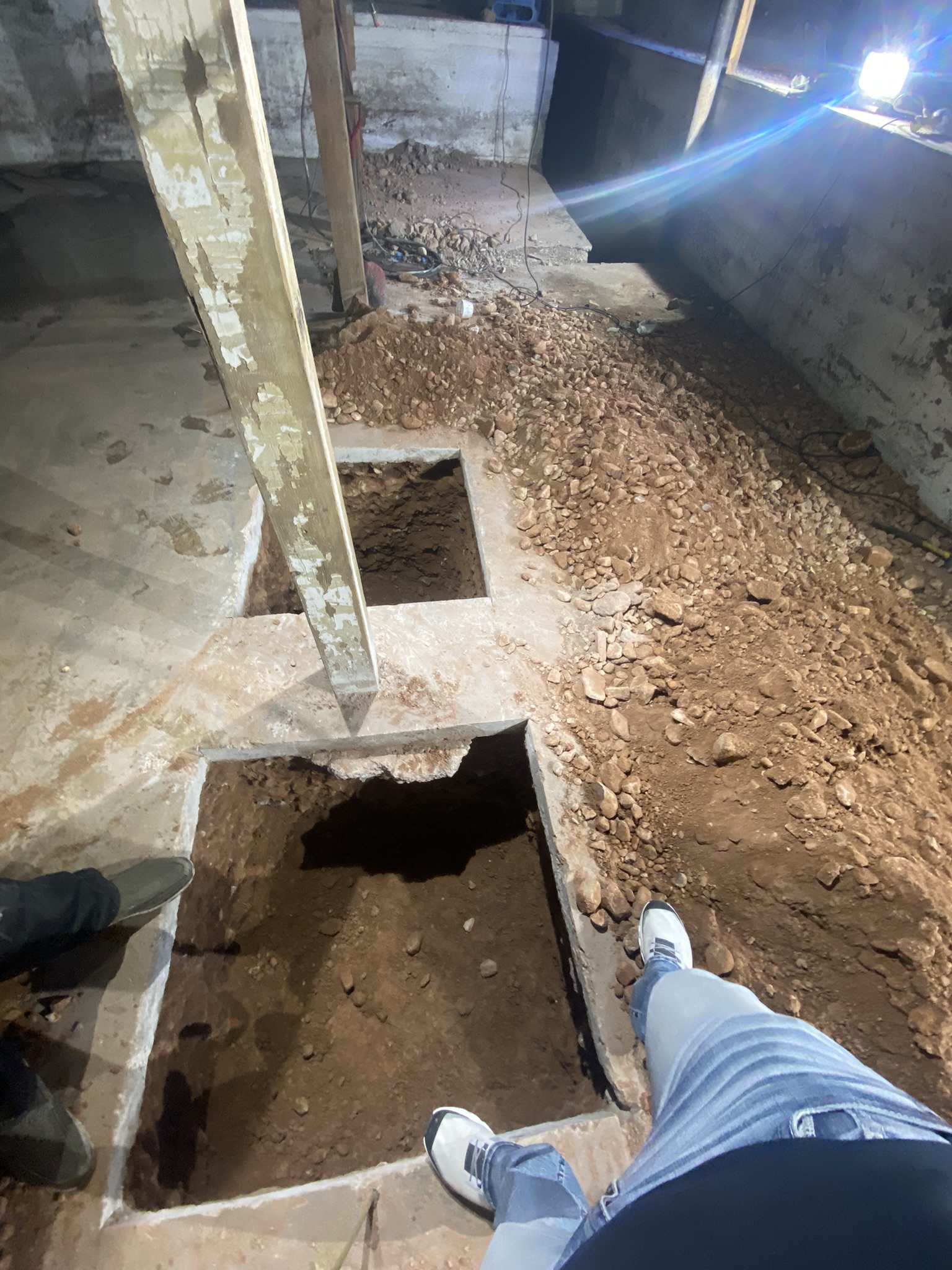 Footing excavation pits viewed from above — concrete slab cut in sections around existing columns for foundation underpinning