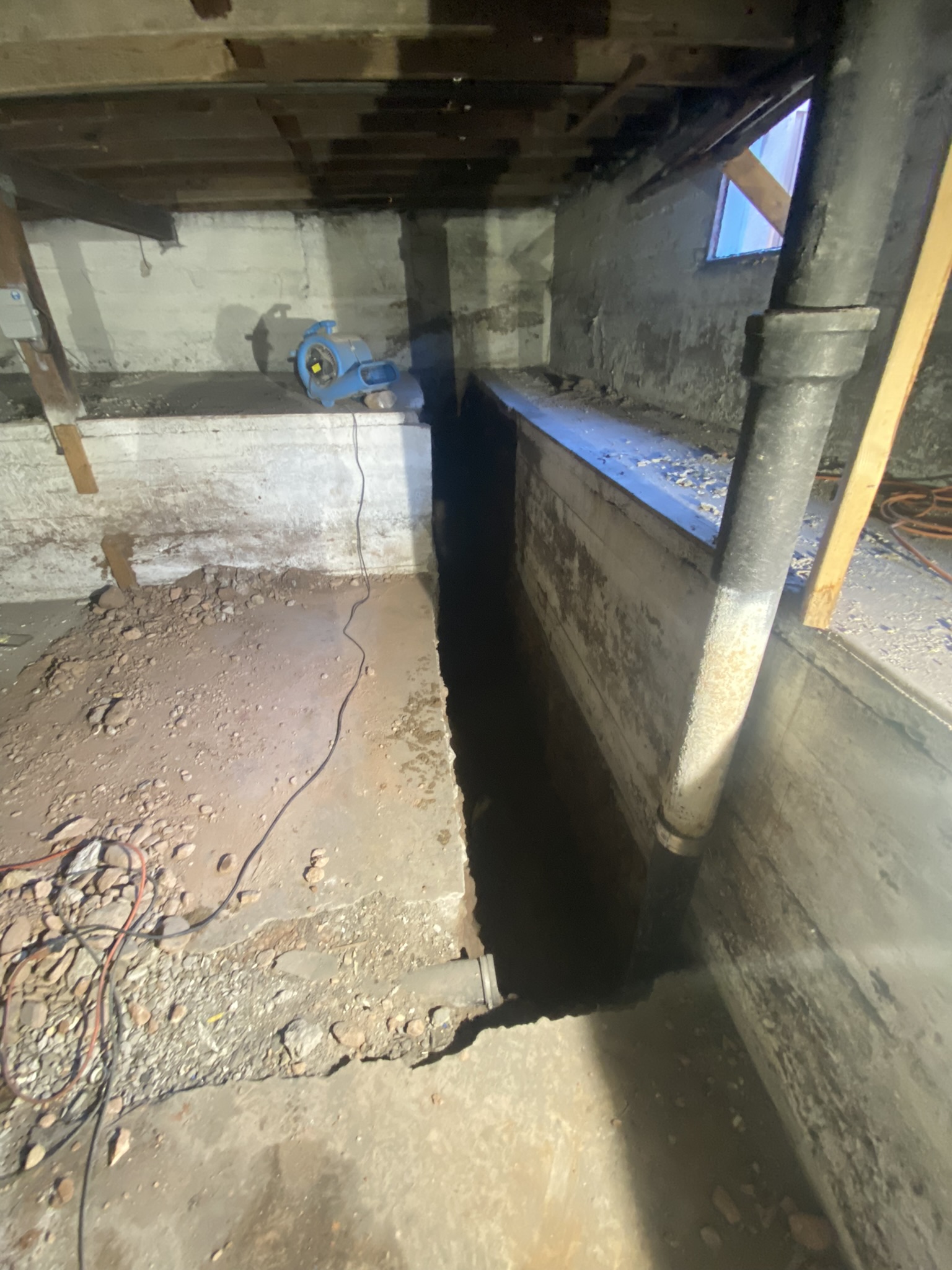 Deep perimeter trench excavated along interior foundation wall revealing moisture damage and failing concrete