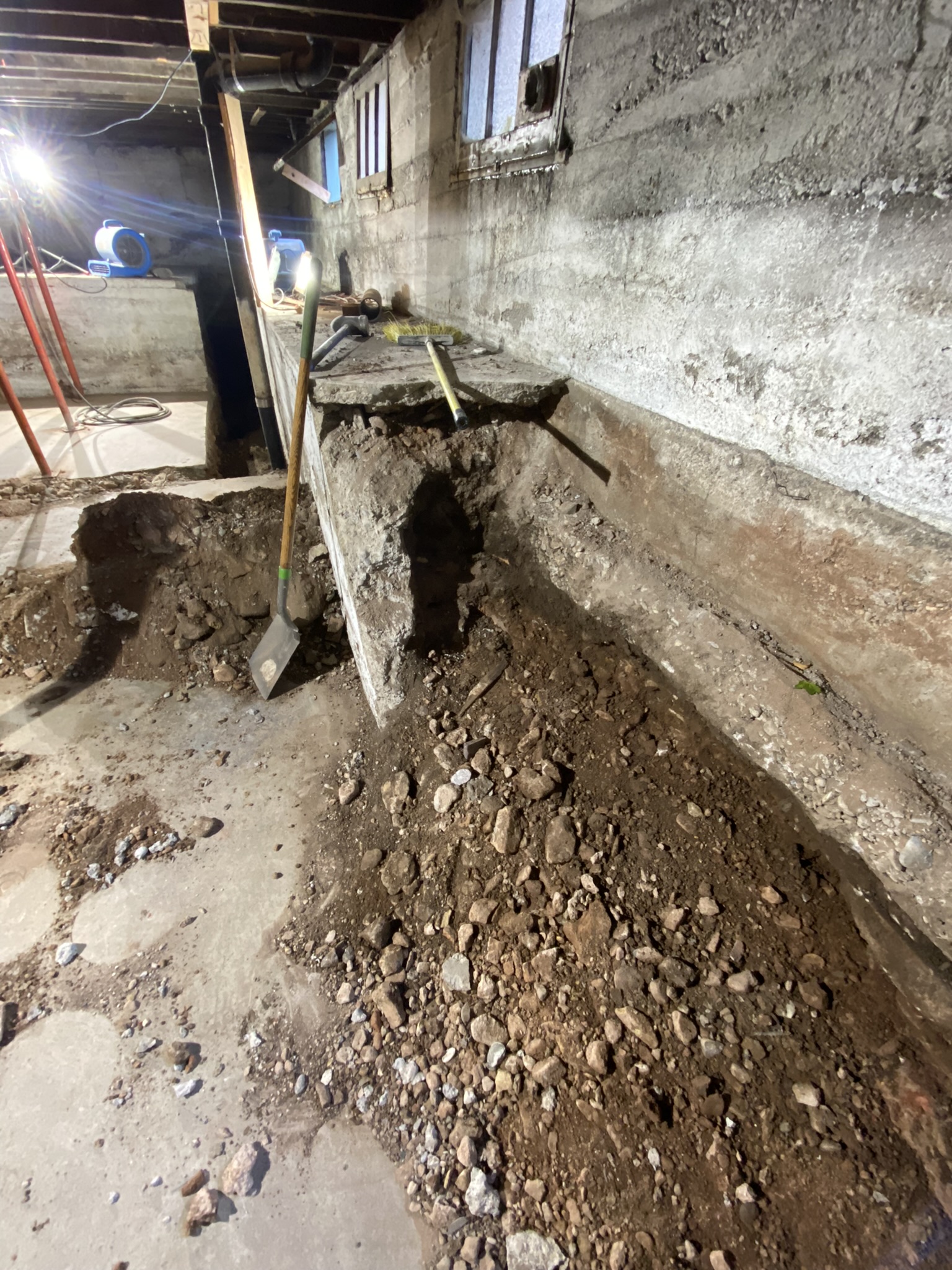 Long perimeter trench along foundation wall with air movers and support jacks — moisture management during structural repair