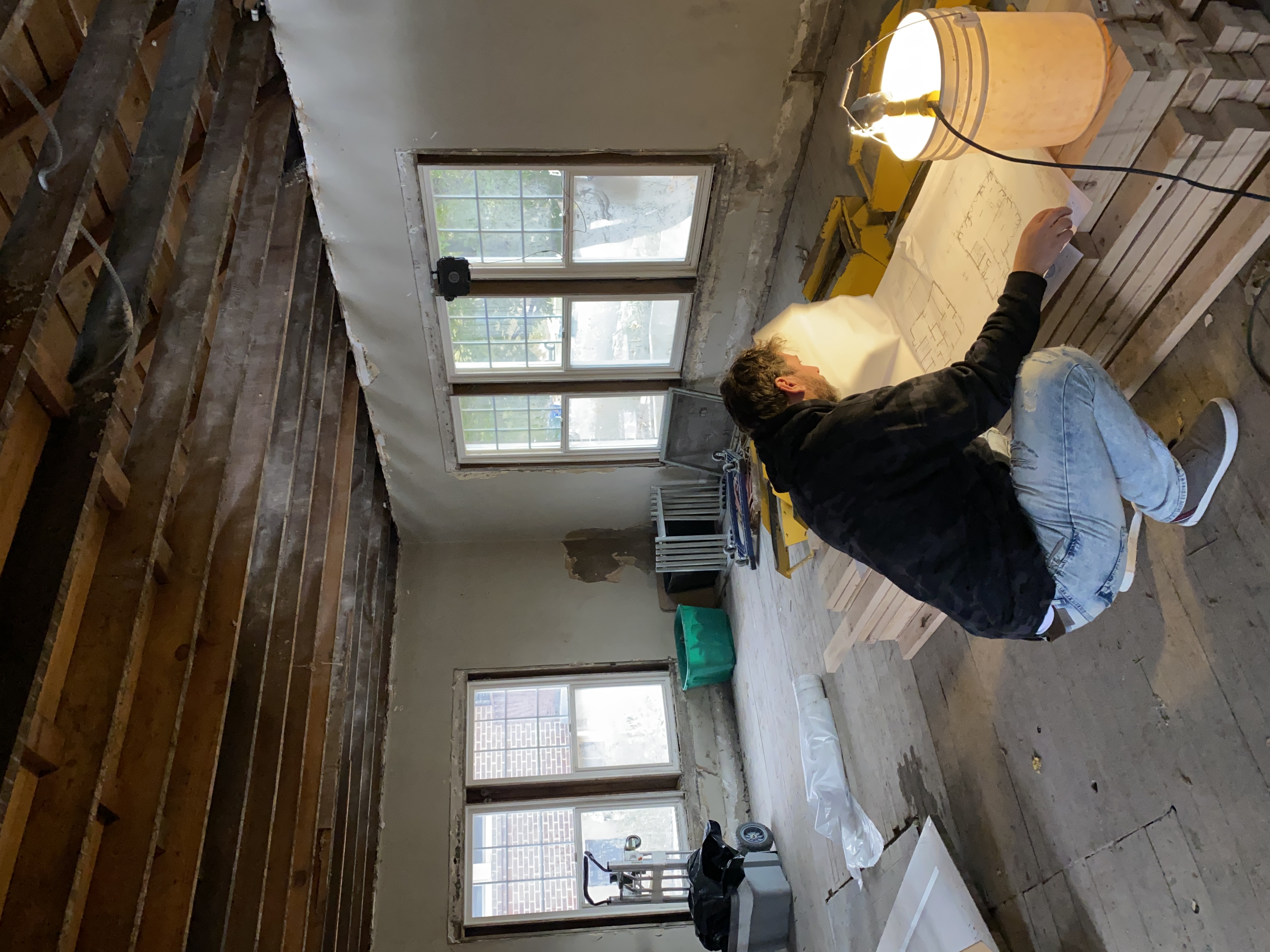 Nate Jensen reviewing structural blueprints inside a gutted older home — exposed ceiling joists and natural light through original windows