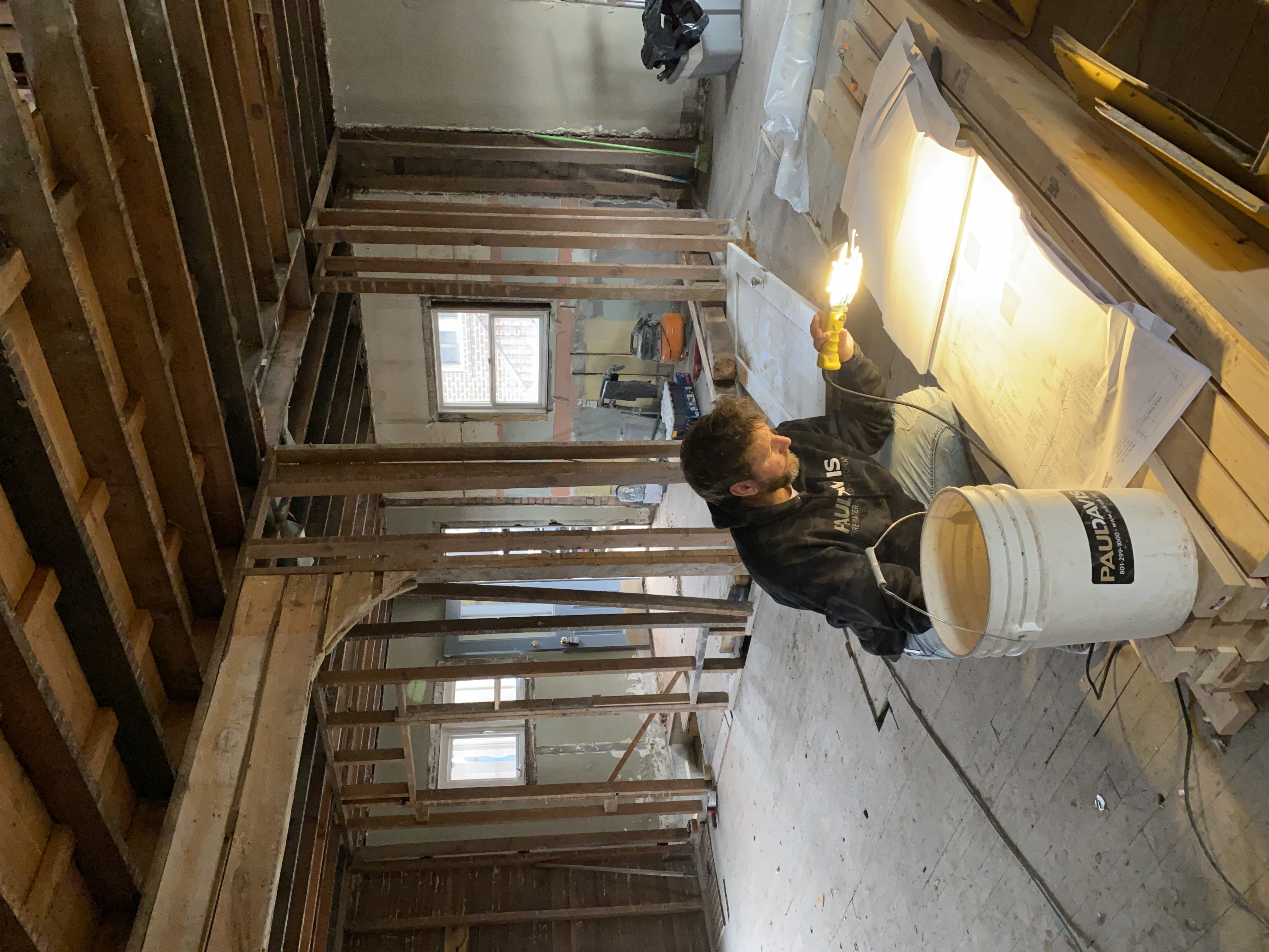 Nate reviewing blueprints by work light in a fully framed room during structural rehabilitation