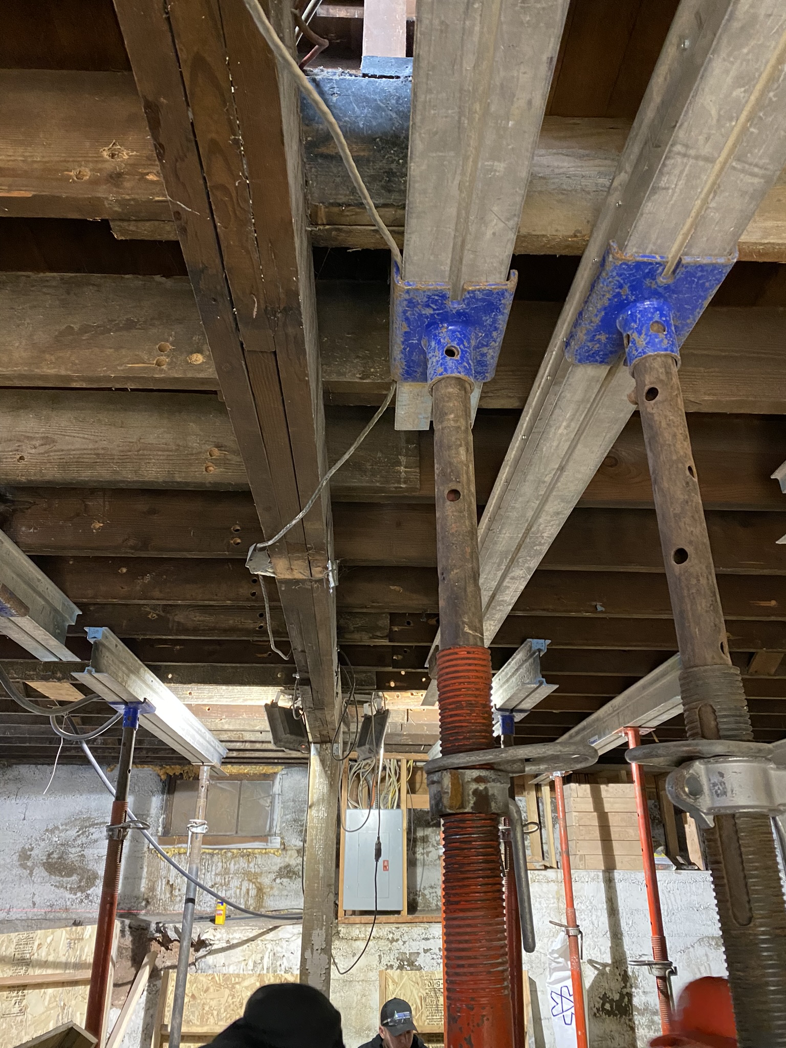 Temporary steel shoring jacks holding up the structure during foundation work — bare concrete and exposed framing