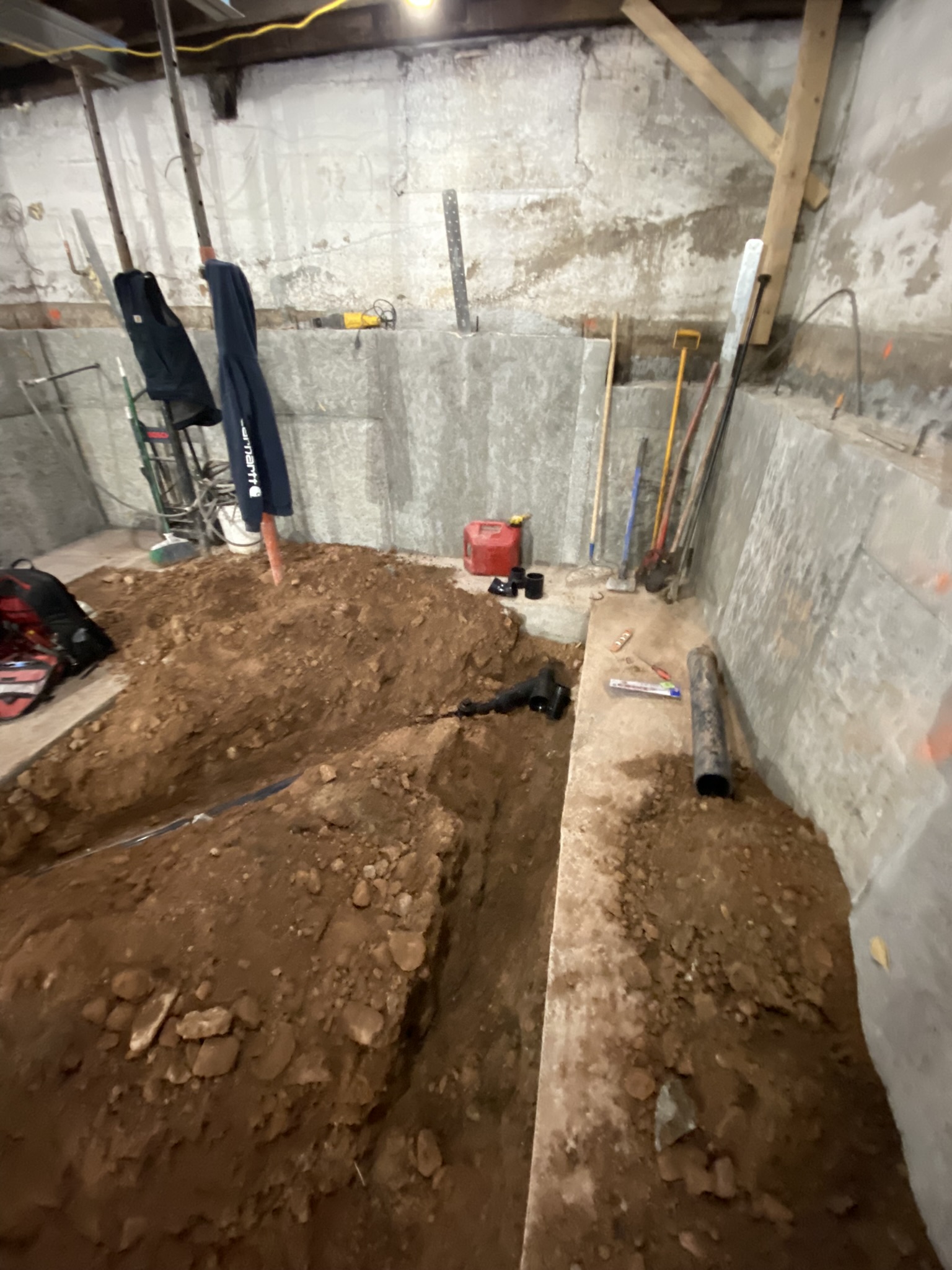 Basement excavation with dirt trenches dug for new footings and plumbing rough-in — ABS pipe visible alongside foundation work