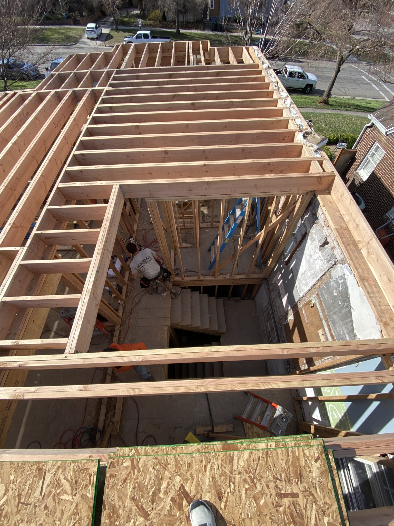 Aerial view looking down from roof level into the framed structure — stairwell, wall framing, original brick exterior visible