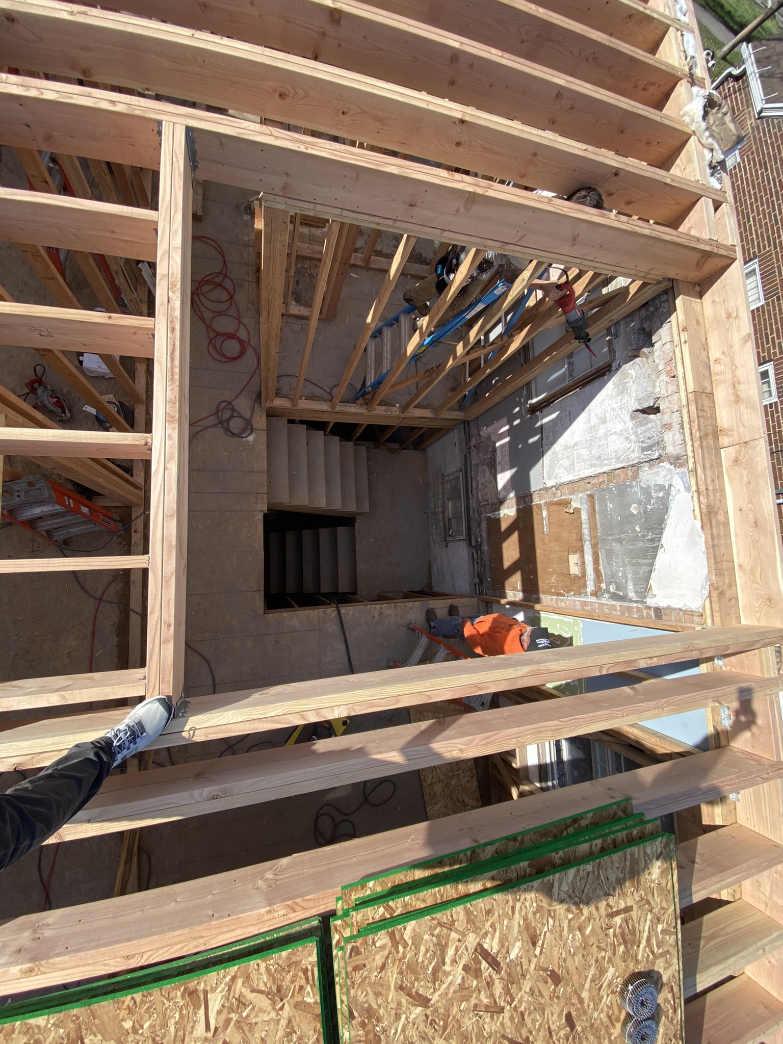 Aerial view showing integration of old concrete block and brick structure with new dimensional lumber framing — workers in orange below
