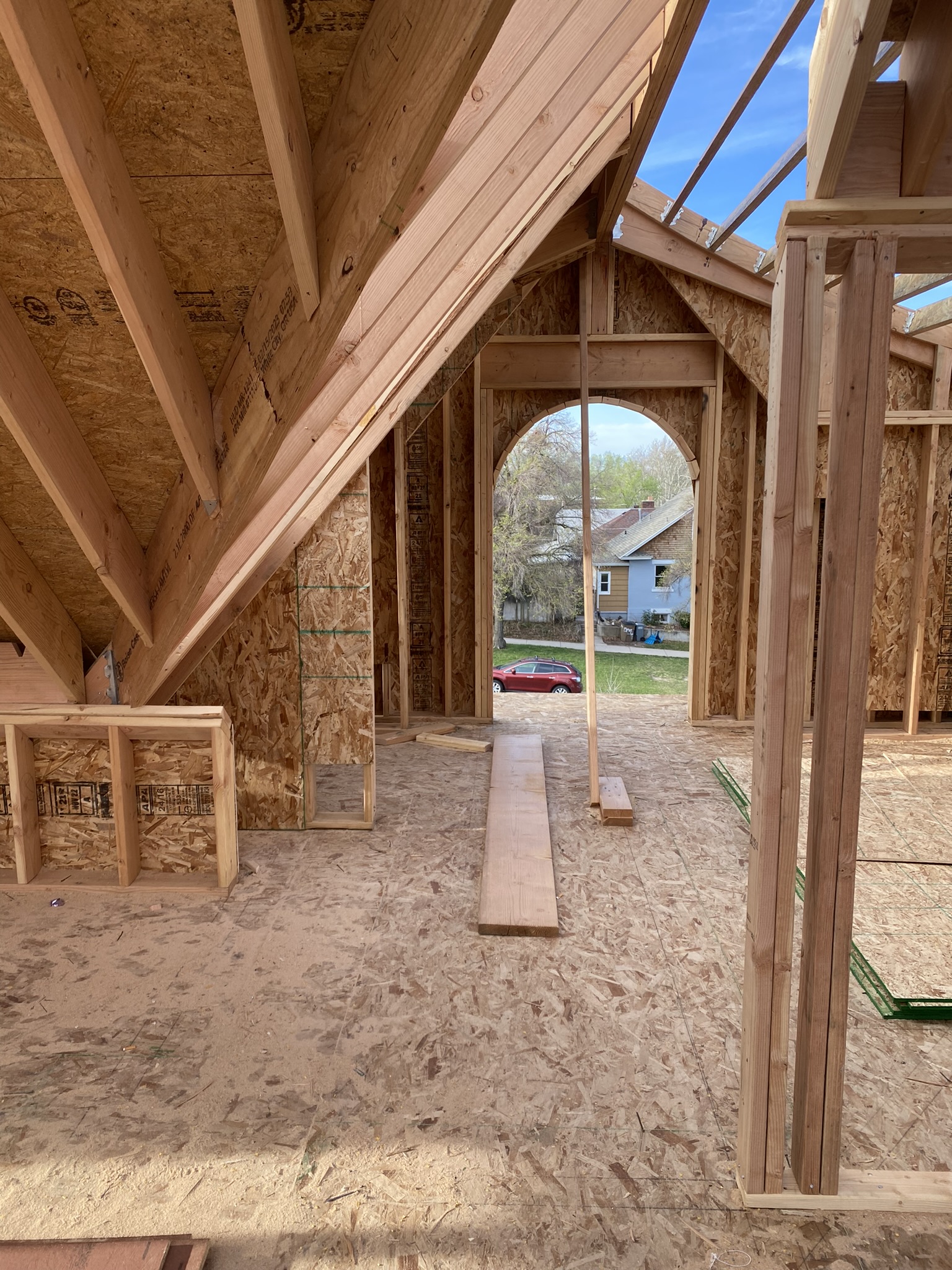 Interior of new upper level looking through arched window opening — roof rafters, OSB sheathing, blue sky visible