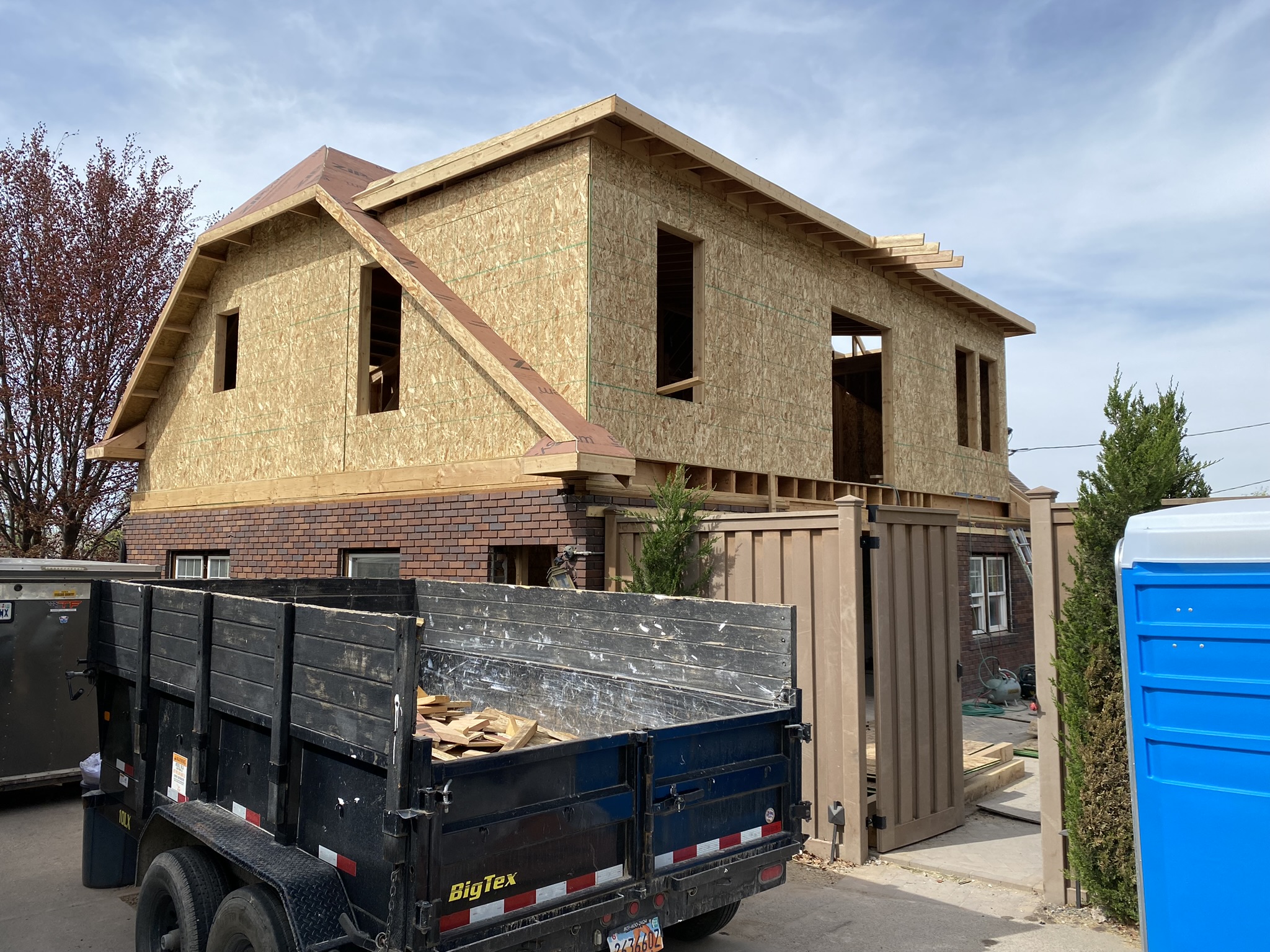 Complete exterior showing new second story addition on top of original brick first floor — multiple roof lines, window openings cut, full structural transformation