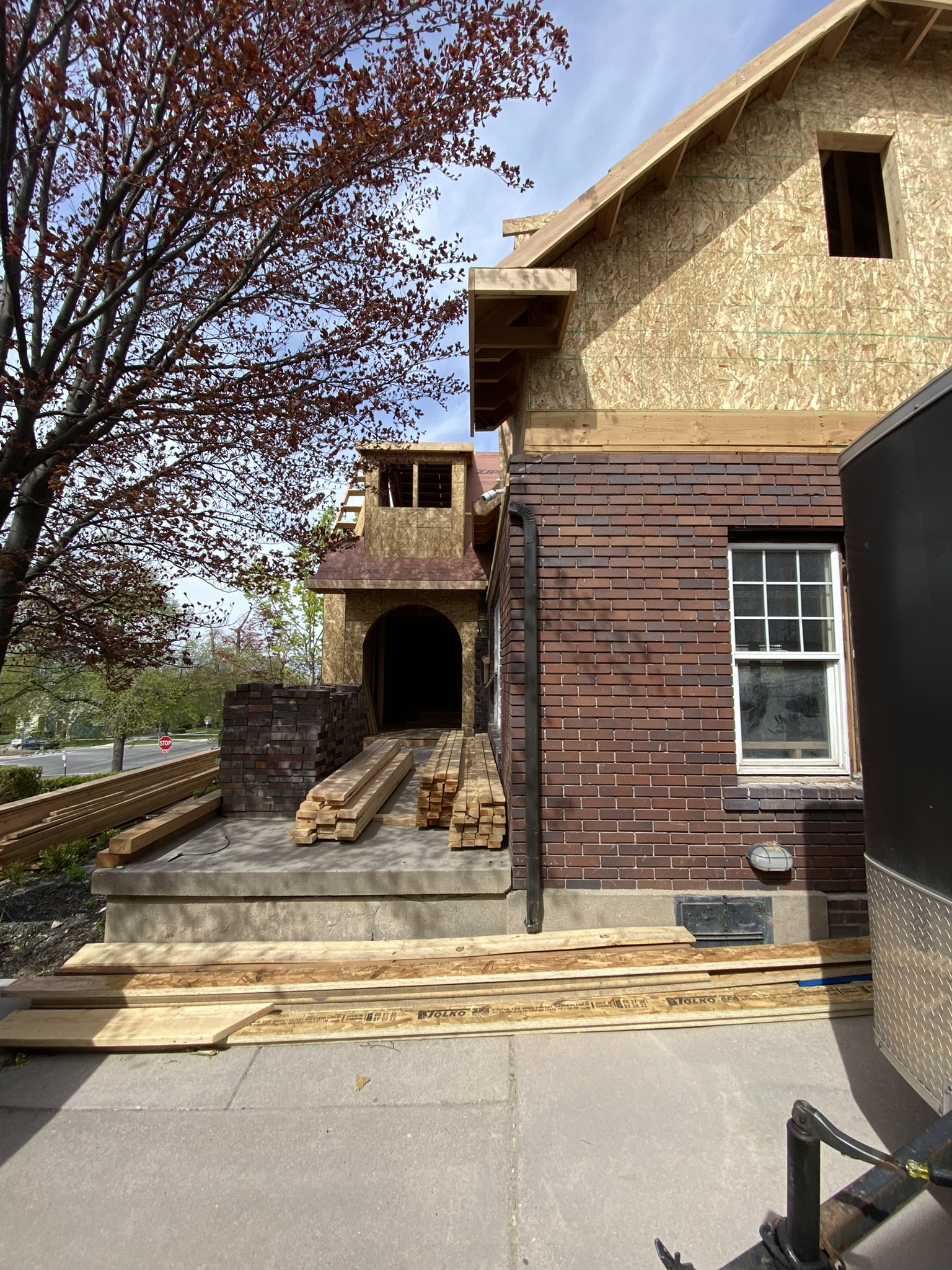 New tower entry addition with arched opening — original brick, lumber stacked on porch, old meets new architectural integration