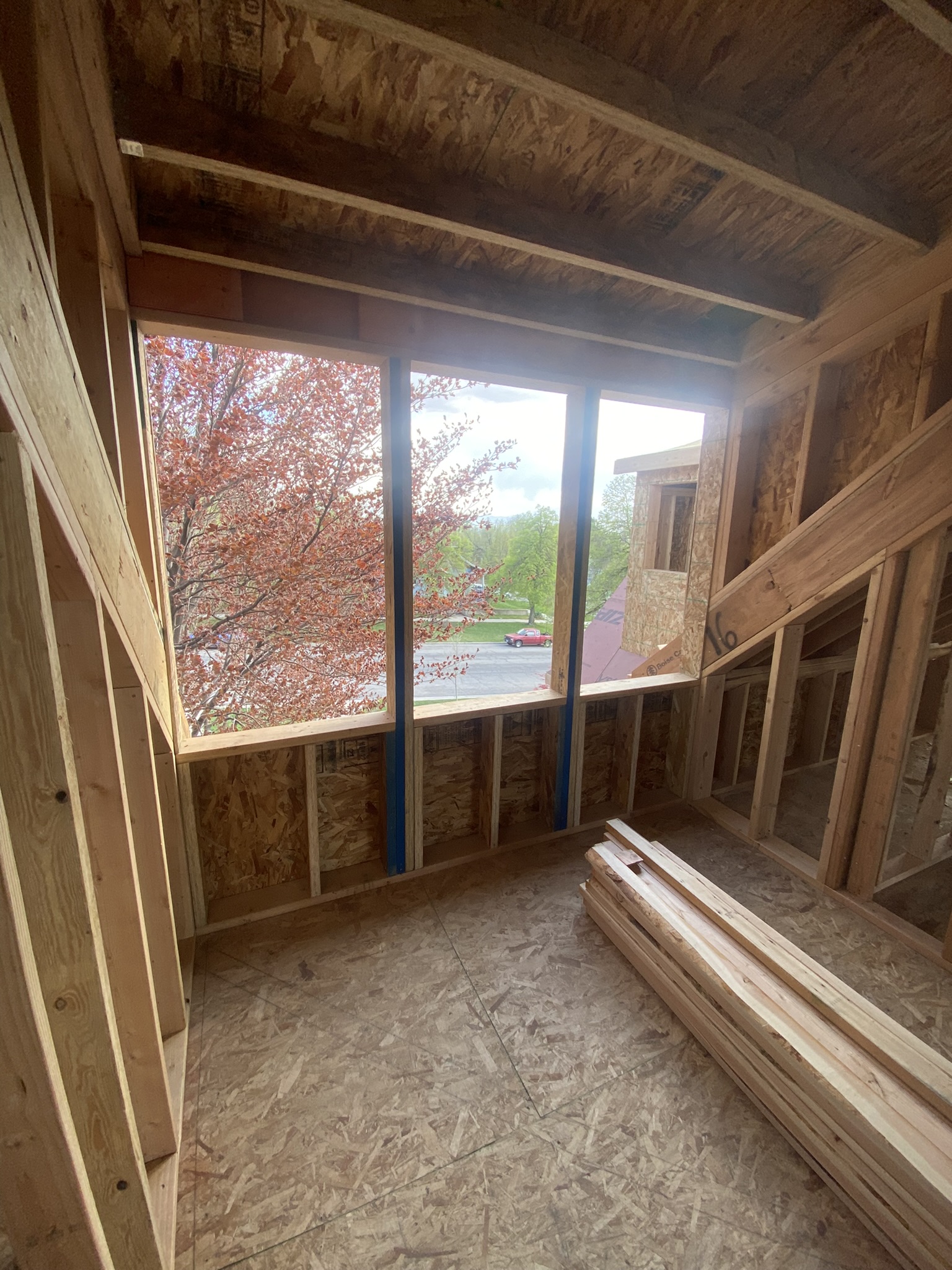 New upper level room with large window openings framed, OSB floor, vaulted ceiling — flowering tree visible outside