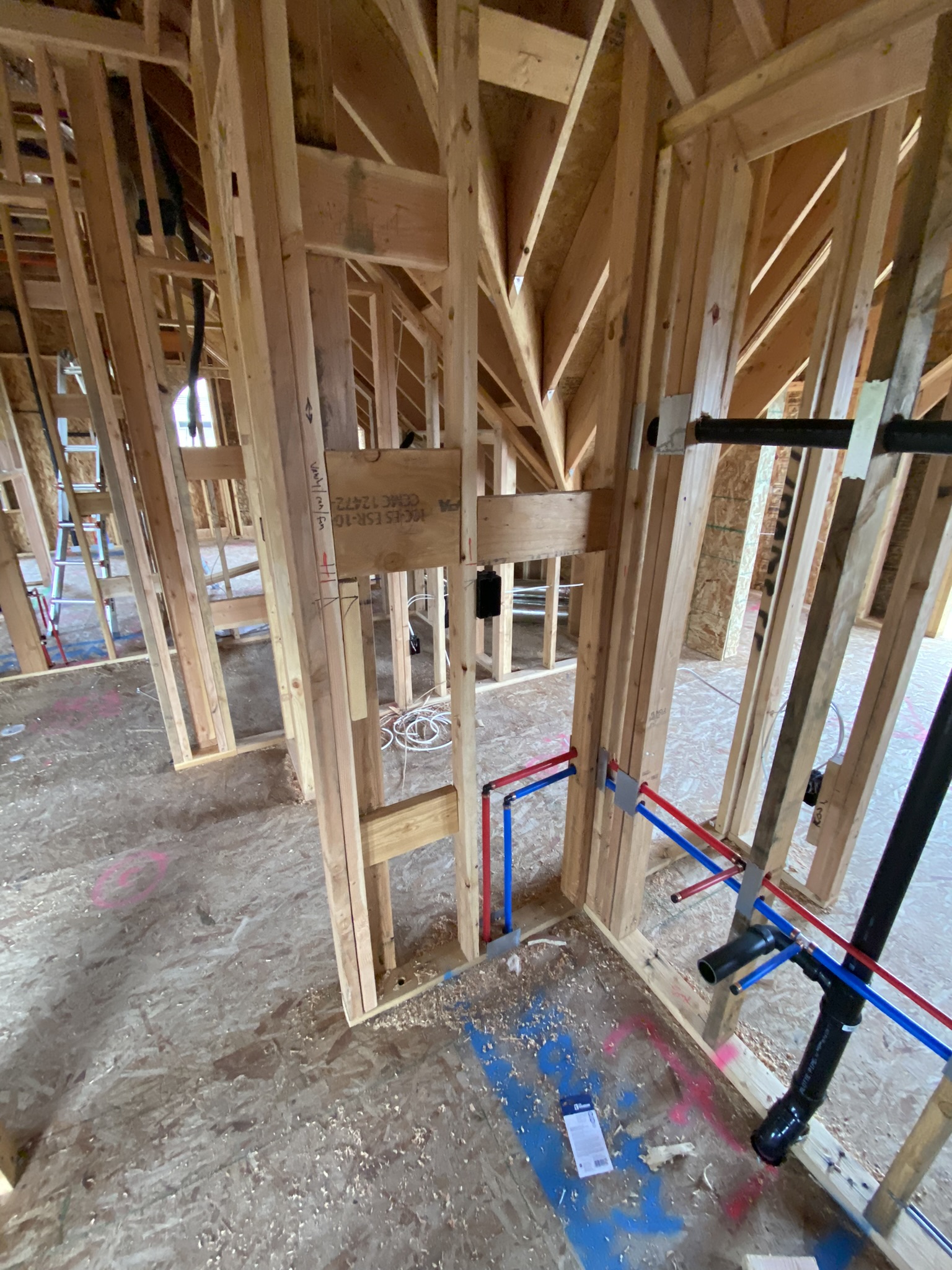 Wide angle of interior framing showing complete MEP rough-in — plumbing, electrical wiring, and HVAC ductwork all visible in open walls