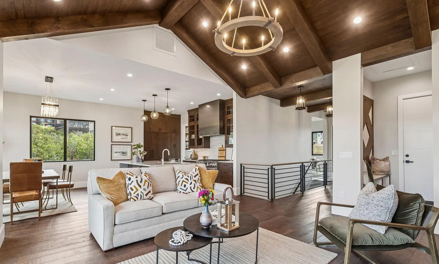 Completed open-concept great room with vaulted ceiling, wood beams, stone fireplace, and chandelier
