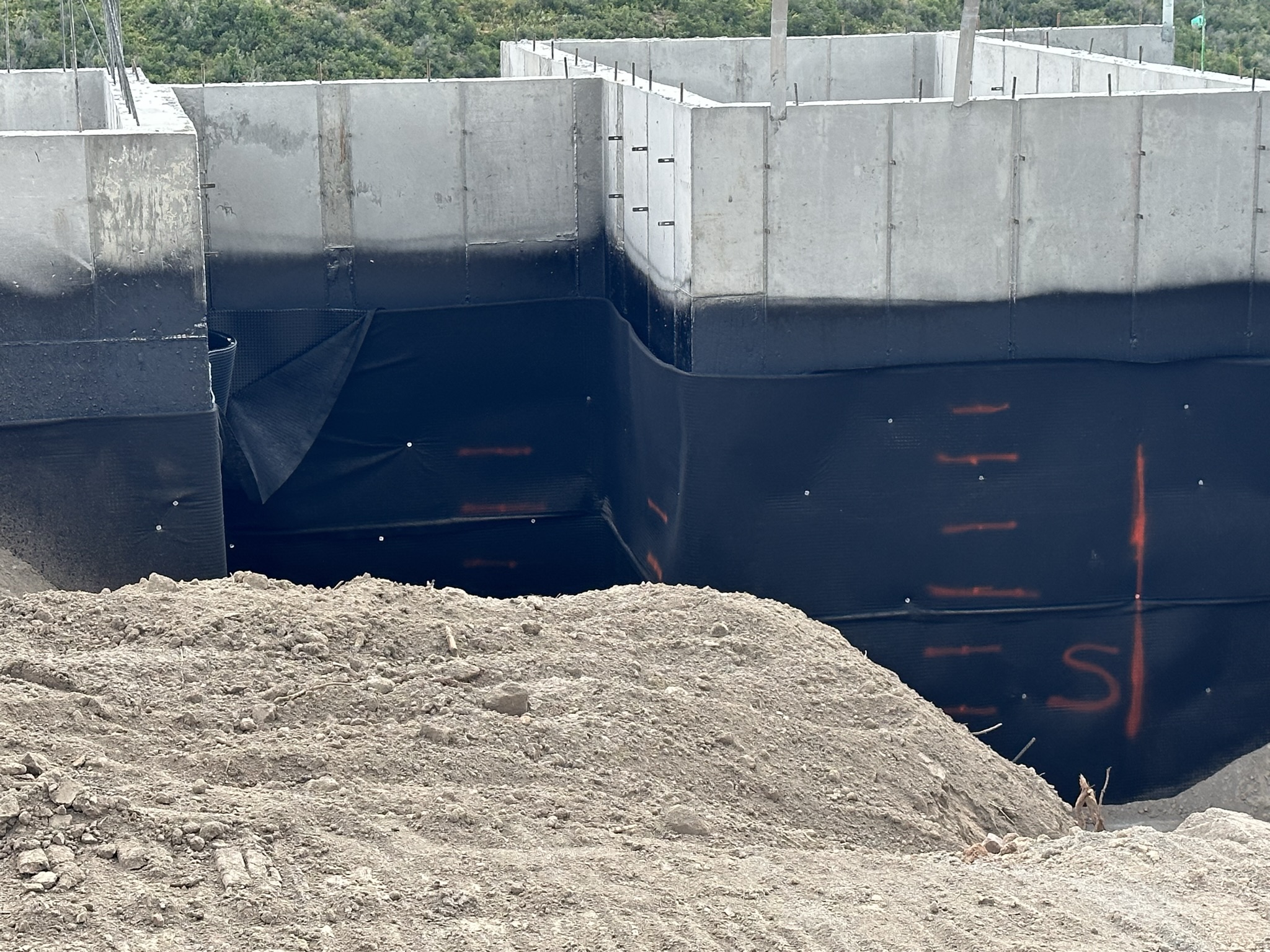Foundation walls with black CCW waterproofing membrane applied below grade before backfill