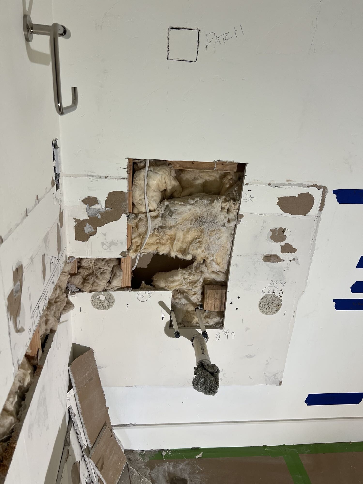 Wall cavity opened to access plumbing and electrical — insulation and framing visible during powder room remodel