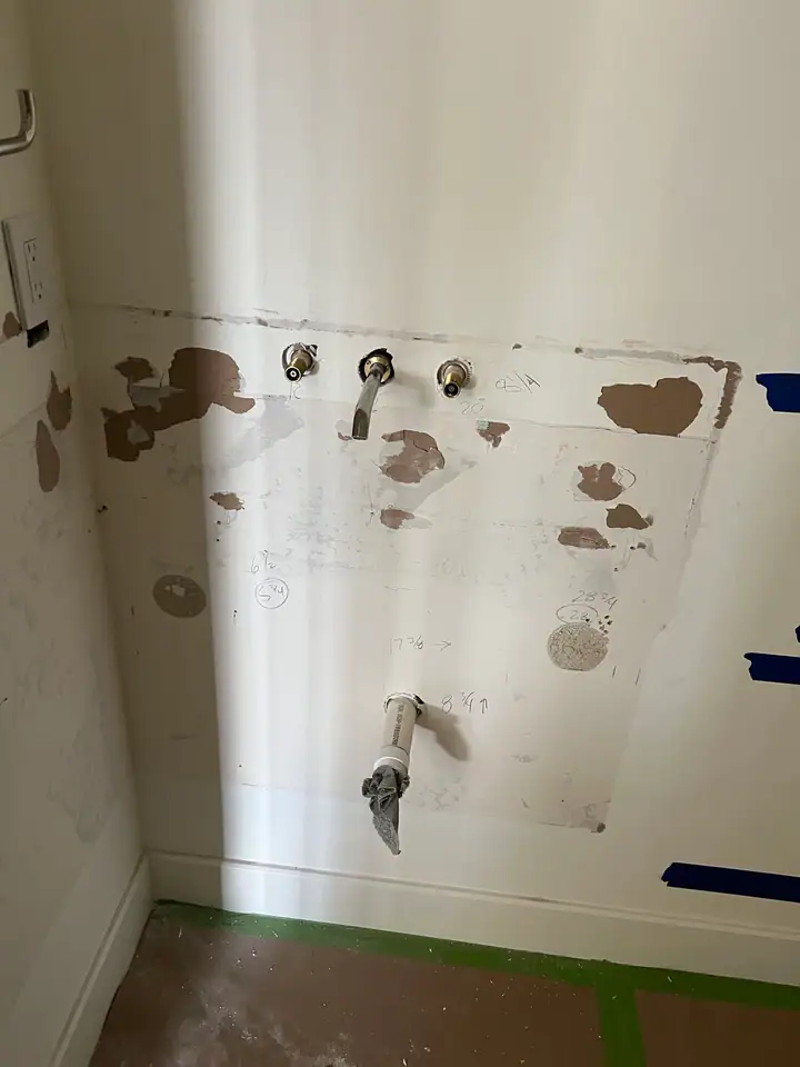 Exposed plumbing and drywall during powder room demolition — supply lines and drain visible before relocation