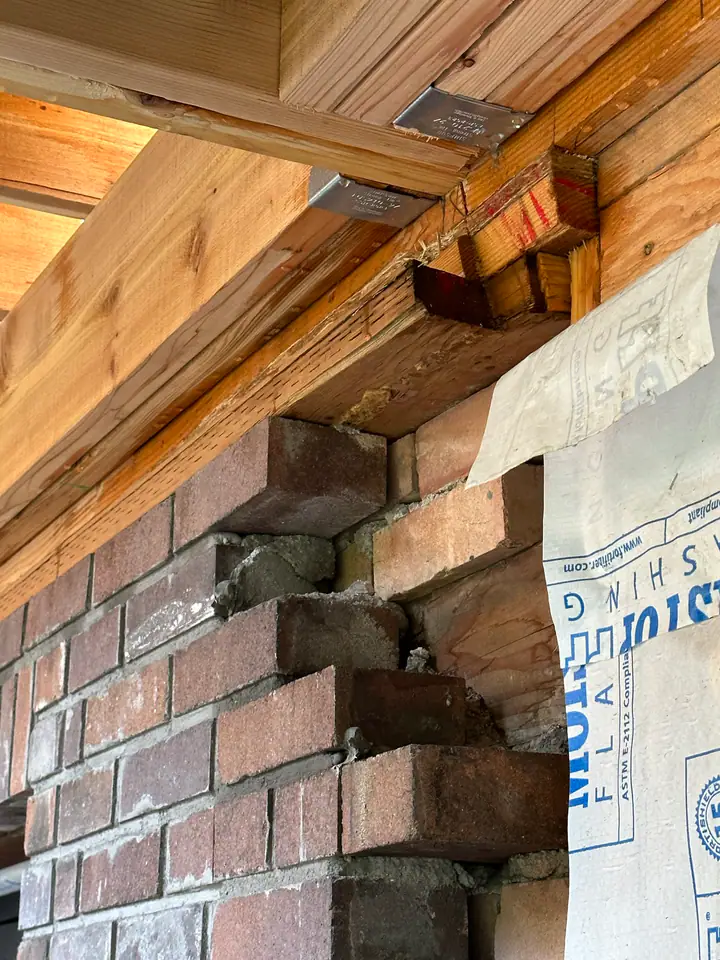 Close-up of new LVL beam connecting to existing brick wall with engineered metal joist hangers — critical structural connection point