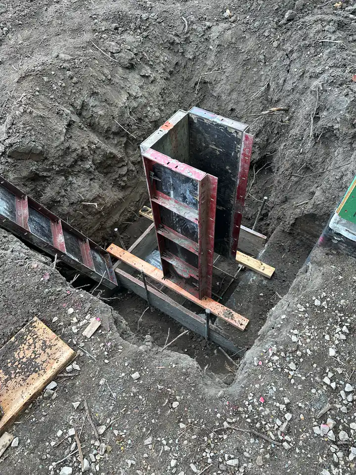 Steel foundation forms set in excavated trench, ready for concrete pour — the first permanent structure on the lot