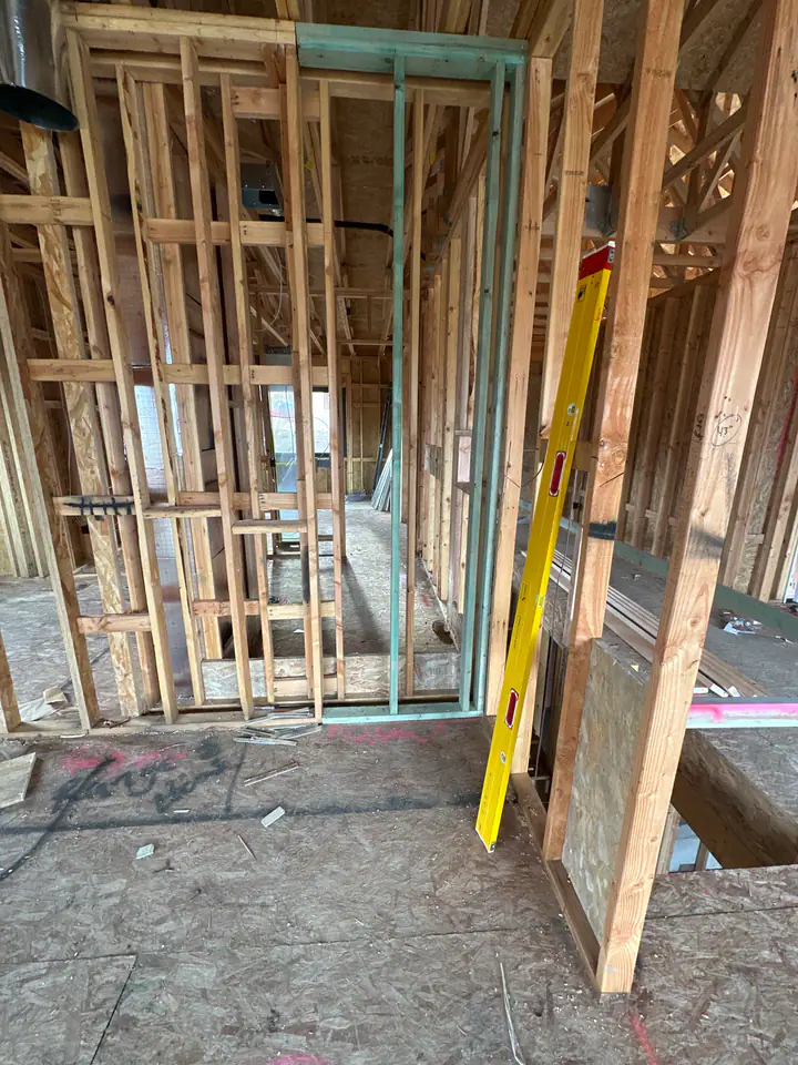 Interior framing detail — stud walls with yellow level, trusses overhead, OSB subfloor