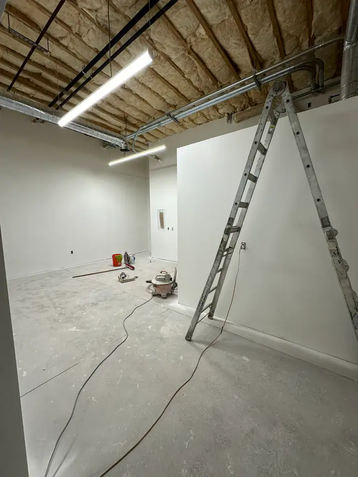 Basement level with drywall hung, HVAC ductwork in exposed ceiling, ladder and tools on concrete floor