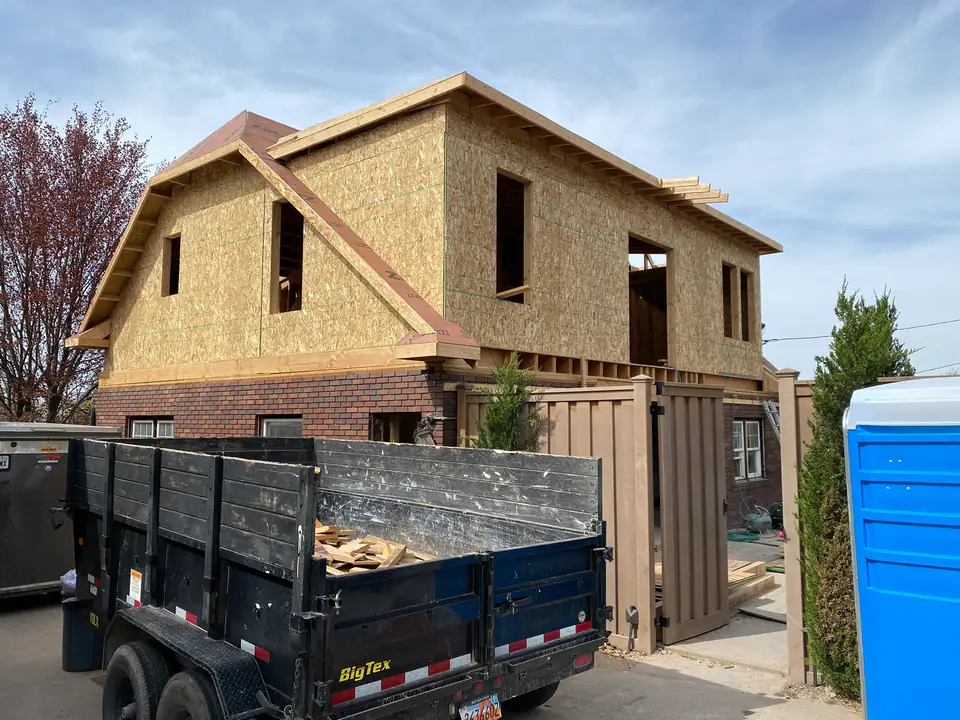 Complete exterior showing new second story addition on top of original brick first floor — multiple roof lines, window openings cut, full structural transformation