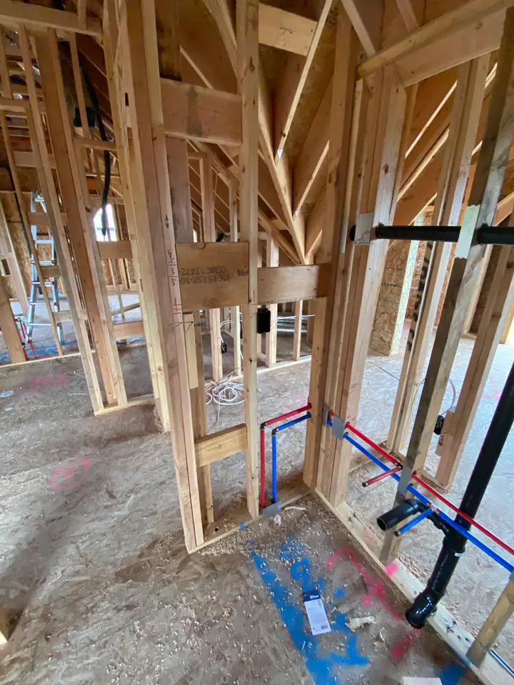 Wide angle of interior framing showing complete MEP rough-in — plumbing, electrical wiring, and HVAC ductwork all visible in open walls