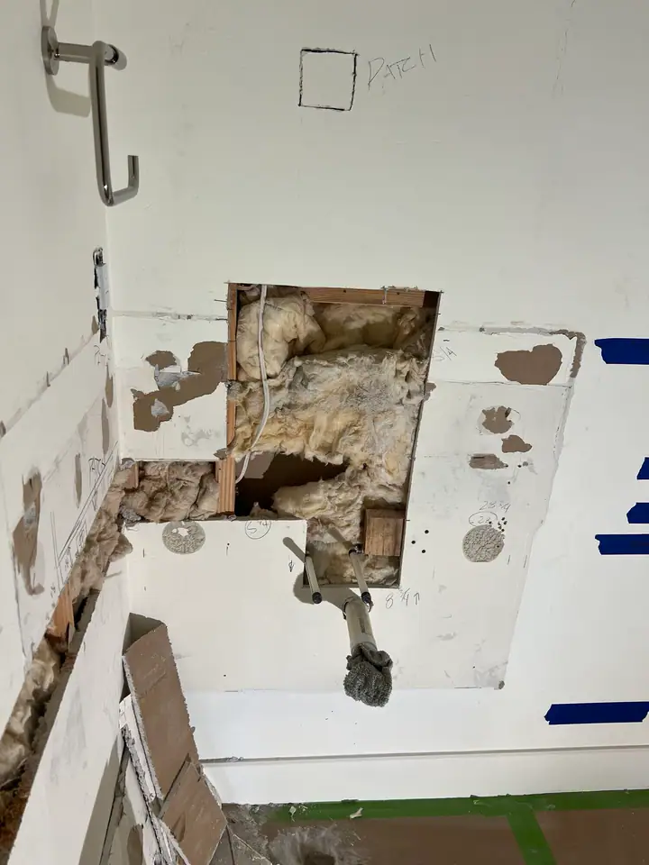 Wall cavity opened to access plumbing and electrical — insulation and framing visible during powder room remodel